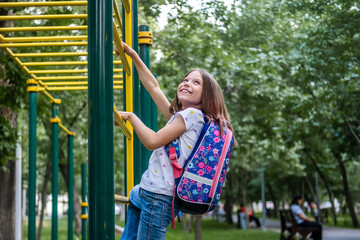 Beautiful school girl with backpack climbing on playground equipment