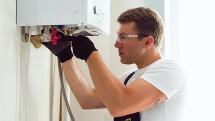 Closeup of plumber using wrench while fixing boiler or water heater, working on heating system in apartment