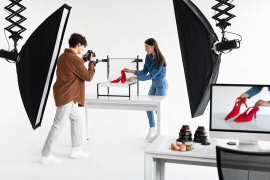 Professional team of man photographer and female assistant taking photos of elegant red shoes, making content photoshoot