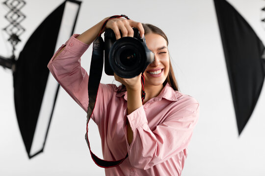 Closeup portrait of young woman photographer taking photo, lady working at studio, using professional dslr camera