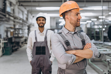 Two international male workers in overalls on the background of the production of PVC windows and doors