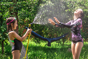 Adorable little girls playing with a garden hose on hot summer day.