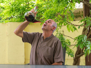 Older man sitting at a table with a glass of red wine in his hand.