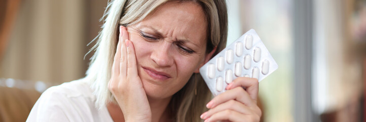 Young woman suffering from tooth pain and holding blister of pills