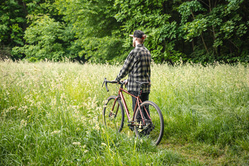 A young man with a bicycle in the forest among the grass.