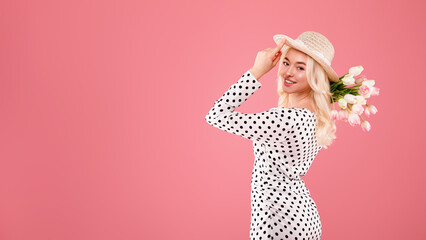 Portrait of happy lady in hat holding bouquet of tupils and smiling at camera over pink background, free space