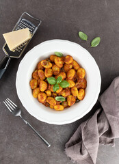 Italian traditional gnocchi with tomato sauce, parmesan cheese and fresh basil on a brown background. Italian food. Copy space.