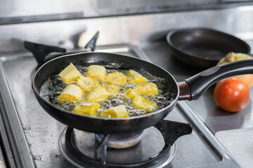 close-up of a frying pan in which green plantains are being fried in pieces to make patacones.