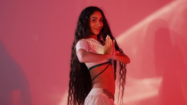 Oriental dance performed by beautiful brunette woman on red background with light effects