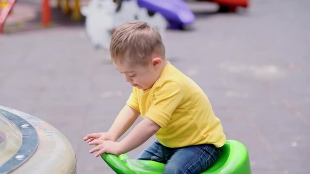 Happy little boy with Down syndrome enjoying riding seesaw at usual children playground adorable preschooler in yellow t-shirt trying new fun activity on summer day