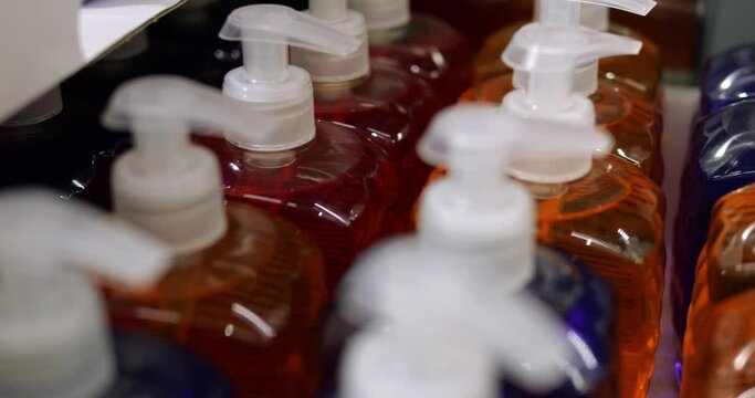 Close-up of unlabeled plastic bottles of red, blue, orange color stand in rows. Generic multicolor liquid cosmetic and body care goods in cardboard box on retail discount store shelf.
