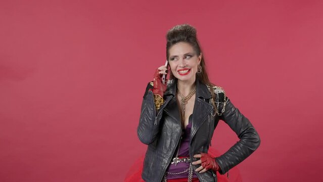 A woman speaks on the phone in a studio on a red background. The woman is embarrassed, flirts, sends a kiss. A woman puts the phone to her chest with a dreamy expression. HDR BT2020 HLG Material.