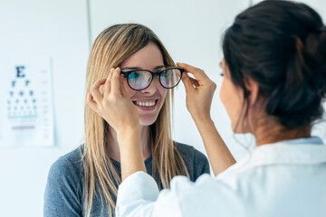 Female doctor choosing while proving eyeglasses to mature beautiful patient in medical consultation.
