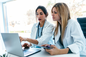 Two beautiful female doctors working with her laptop while talking in the medical consultation