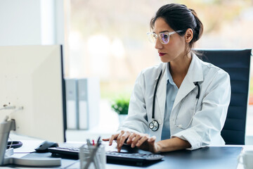 Beautiful female doctor working with computer in medical consultation.