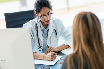 Beautiful cheerful female doctor talking while explaining medical treatment to patient in the...