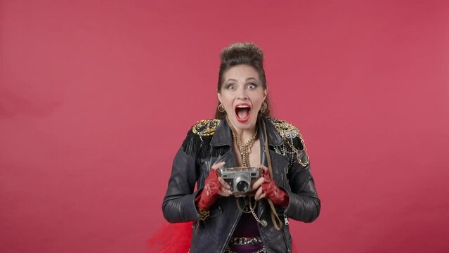 A woman passes with a vintage camera, stops abruptly, takes a lot of shots on the camera. The woman joyfully jumps in place, runs away. Woman in the studio on a red background. HDR BT2020 HLG Material