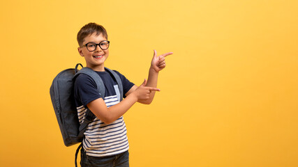 Happy boy schooler pointing at copy space, isolated on yellow