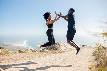 Young black couple jumping and giving high five, enjoying workout together in morning on rocks at ocean, outdoors