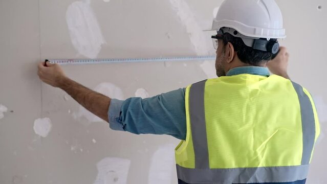 Construction worker measuring shabby wall near hanging wires preparing for socket installation focused specialist helping owners with renovation of house interior