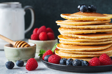 Delicious pancakes, with fresh blueberries, raspberry and maple syrup or honey on a dark background