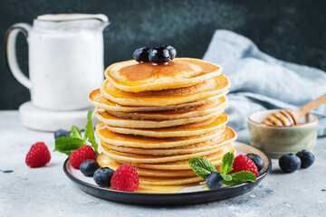 Delicious pancakes, with fresh blueberries, raspberry and maple syrup or honey on a dark background