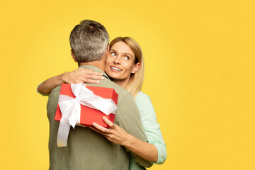 Family holiday concept. Happy woman holding gift box and hugging husband, looking aside at free space