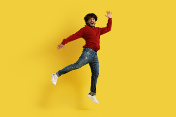 Fototapeta na wymiar Excited thrilled millennial indian guy jumping over yellow background
