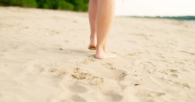 Woman feet walking barefoot on sandy beach of sea
