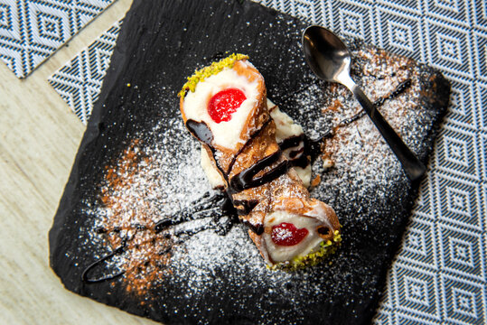 Italian Sicilian cannolo pastry dessert closeup on black stone plate macro with texture of yellow crust and ricotta cheese and pistachio cream filling with chocolate chips in cannoli