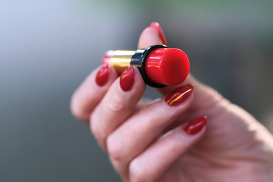 Red lipstick in female hand with red manicure, hand with lipstick