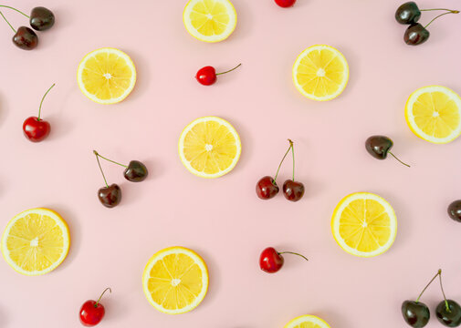 Creative fruit pattern made of red cherries and yellow lemon slices on light pastel pink background. Minimal cherry fruit and citrus layout. Nature summer pattern concept. Flat lay summer food idea.