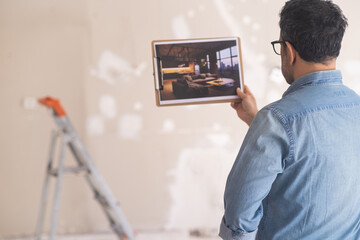 Man in glasses looking at picture with loft-style interior design standing in unfinished room against ladder and shabby wall home owner ready for renovation in apartment