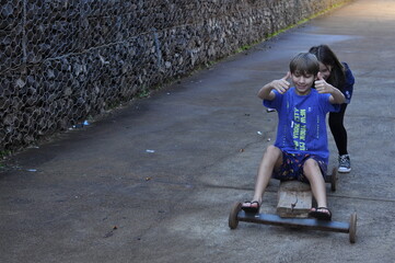 crianças menino e menina brincando com carrinho rustico na rua, infância simples divertida e...