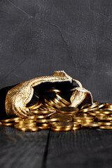 A bag with gold coins on a wooden background. The money is in a black bag. Treasure Hunt. A Purse with money on a black background. Wallet wit gold coins.Copy space