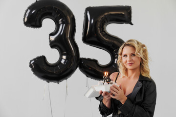 blonde woman in black with a cake with a candle number thirty-five