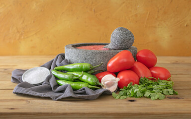 Mexican red sauce in a molcajete white fresh ingredients around on rustic surface. 