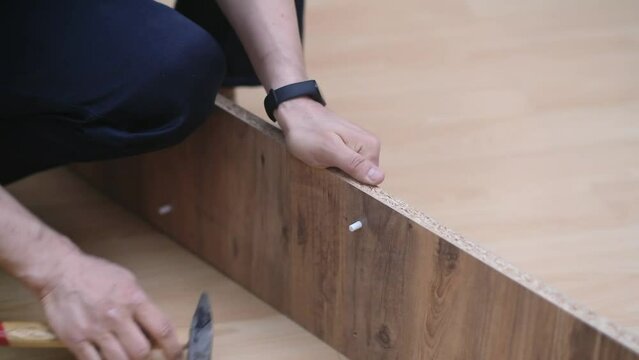 Furniture manufacturing and shipping specialist hammering shelf holders into wooden rack sitting on floor in apartment professional woodwork for interior design