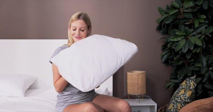 A Woman Sits On A Bed After Changing The Sheets For New Ones. A Girl Sniffs A Clean Smelling Pillowcase That She Washed With New Laundry Detergent, Softener.