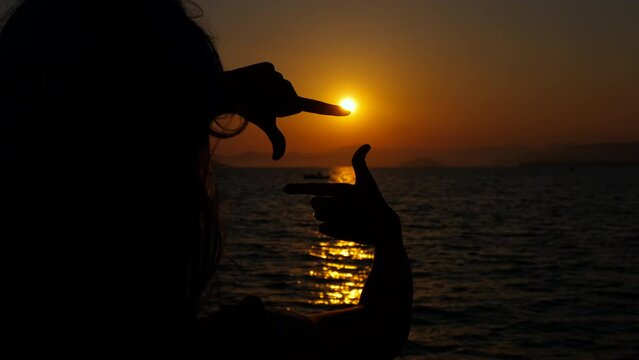 Silhouette girl making hand frame by sea. A child silhouette making hands frame to make a photo on orange sun on the nightfall beach in summer.