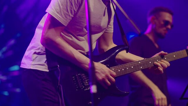 A virtuoso guitarist playing an electric guitar on stage with flashing neon lights. Man is playing guitar on stage. Young man playing on electric guitar