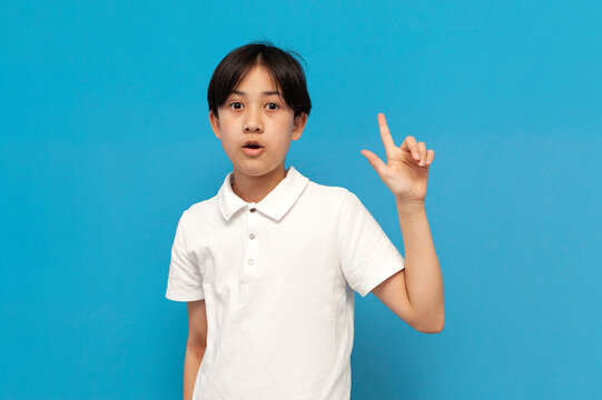 I Have An Idea. Asian Boy Of Twelve Years Old Pointing His Finger Up And Came Up With Idea On Blue Background