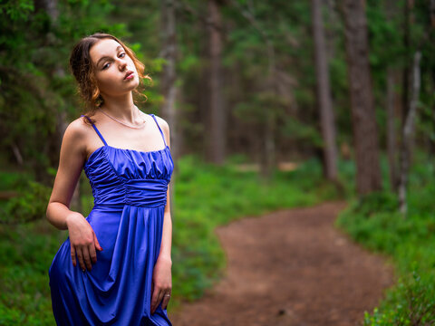 Teenager girl in a blue high fashion dress posing on a footpath in a forest. Senior prom pictures. Glamour and elegance concept. Model in designer clothes.