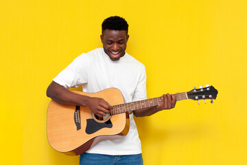 joyful african american man holds acoustic guitar and sings on yellow isolated background