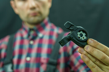 Portrait of a young mechanic in a plaid shirt on a black background in the process of work. A bicycle mechanic holds a tool and a spare part for a mountain bike in his hands. Replacing the shifter
