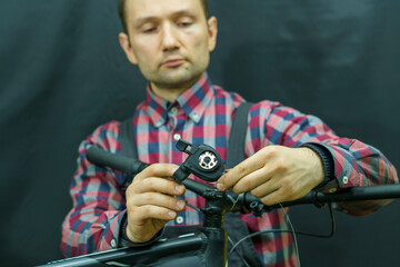 Portrait of a young mechanic in a plaid shirt on a black background in the process of work. A bicycle mechanic holds a tool and a spare part for a mountain bike in his hands. Replacing the shifter