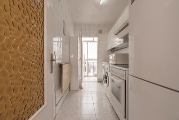 Old kitchen with mismatched white cabinets, white square tiles, exit to a terrace and a wooden folding