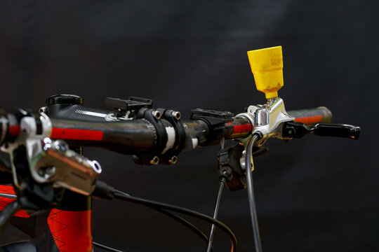 Bleeding the brake system of a mountain bike with a funnel. Bicycle repair. A mountain bike handlebar and modern disc hydraulic brakes on a black background.