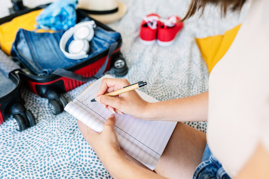 Close up view of young woman hands preparing travel summer check list on bed. Holidays lifestyle concept.