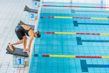 Professional female swimmer preparing and jumping off the starting block into the pool. Competitive...